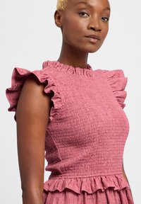 Roze textuur jurk met ruches mouwen, een gefronste halslijn en een peplum detail bij de taille. De stof is zacht met een gekreukt patroon.
