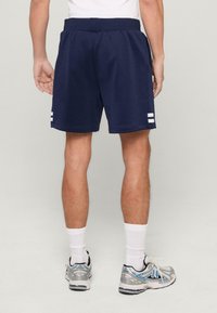 Jūrų paleidimo šortai su minkšta tekstūra, elastinga juosta ir dviem baltomis linijomis šoninėse pusėse. Dėvimi su baltais sportiniais kojiniais ir sidabriniais sportbačiais.