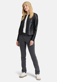 Svart faux läderjacka med rundad nederkant, dragkedja, bärs över en vit skjorta. Grå slim-fit jeans och vita sneakers fulländar outfiten.