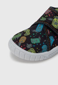 Svart stoffsko med fargerike mønstre av spillkonsoller og kontrollere, med en grå gummisåle og oransje søm-detaljer.