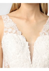 White lace dress featuring floral embroidery, a deep V-neckline, and sheer details along the straps. Textured fabric with delicate accents.