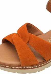 Sandalia de ante naranja con un diseño de tiras entrelazadas, plantilla acolchada y suela de goma beige con detalles de costura.