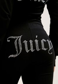 Mustad mustad, millel on rhinestone ehted sõnaga "Juicy". Materjal näeb välja pehme ja siledapinnaline. Kujundus on keha järgiv.