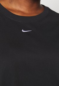 Närbild av svart crew neck-t-shirt med liten vit Nike-swoosh-logotyp centrerad under kragen.