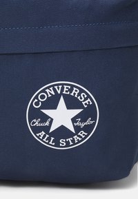 Bolsa de lona navy con un logo circular blanco que presenta una estrella, con la inscripción "CONVERSE ALL STAR" y "Chuck Taylor", y con costuras en contraste.