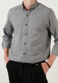 Grijze overhemd met knopen gemaakt van gestructureerde stof, met een verspreide kraag, lange mouwen met opgerolde manchetten en donkere knopen.