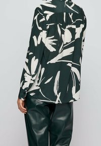 Blouse à motif abstrait vert et blanc, avec des manches longues et une coupe décontractée, dotée de poignets à boutons et d'un dos plissé.