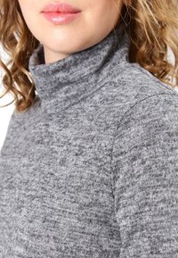 Grauer Rollkragenpullover aus weichem, strukturiertem Stoff mit lockerer Passform, der eine gerippte Kragen- und Schulternahtverarbeitung zeigt.