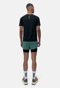 Juoda sportinė marškinėliai trumpomis rankovėmis, derinami su žaliais šortais. Išskirtinė atspindinti detalė marškinėlių gale. Baltos ir juodos dryžuotos kojinės.