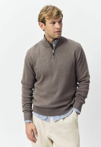 Brązowy sweter z zamkiem, wykonany z dzianiny, z prążkowanymi mankietami i dołem, noszony na niebieskiej i białej koszuli w paski.