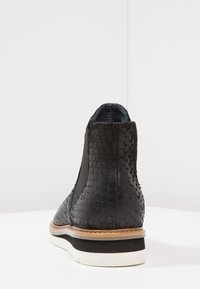 Botas Chelsea negras con un patrón de serpiente texturizado, paneles laterales elásticos y una suela blanca contrastante.