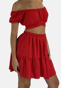 Ensemble rouge deux pièces comprenant un top à épaules dénudées et une jupe à volants. Confectionné en tissu léger avec une finition douce et texturée.