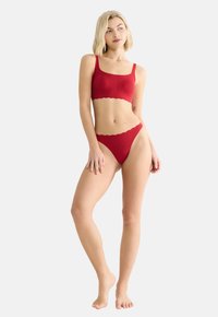 Bralette rouge à côtes et string assorti, avec des bords festonnés et une texture douce. Conçu pour un look ajusté, avec des bretelles réglables.
