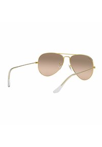 Occhiali da sole aviatori oro con lenti marroni sfumate, montatura in metallo e puntali in plastica trasparente. Design classico e accattivante per la protezione dal sole.