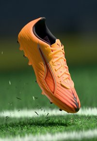 Lyseorange fodboldstøvle med tekstureret overdel, sorte detaljer og snørebånd. Har et let design og formstøbte knopper for bedre greb.