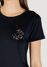 Czarna bawełniana koszulka z okrągłym wzorem zrobionym z kryształków na klatce piersiowej, z klasycznym okrągłym dekoltem i krótkimi rękawami.