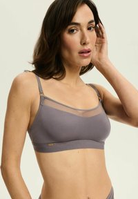 Graue Bralette mit oberem Netzpanel und solidem unteren Abschnitt. Verfügt über verstellbare Träger und feine Hardware-Akzente. Glatte Stofftextur.