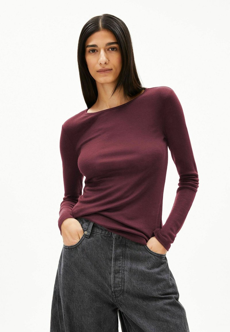 Bordeauxrotes Langarmshirt aus weichem Stoff mit einem Bootsausschnitt, kombiniert mit hoch taillierten, locker sitzenden dunkelgrauen Jeans.