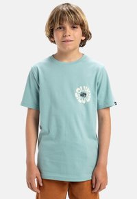 Camiseta de algodón azul claro con mangas cortas y cuello redondo, que presenta un logo gráfico blanco en la parte delantera.