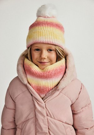 Strikket beanie med gule, pink og hvide striber, toppet med en hvid pom pom, parret med en matchende stribet cowl, båret over en pink jakke.