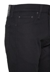 Black denim jeans with a slim fit, featuring metal hardware, standard back pockets, and subtle stitching detail. Smooth texture throughout.