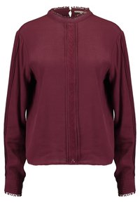 Blouse bordeaux à manches longues avec un col haut, un panneau frontal texturé et une bordure décorative le long des poignets. Tissu lisse avec un léger brillant.