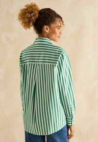 Langärmliges Hemd in Grün- und Weißstreifen mit einem Rückenschlitz, Knopfmanschetten und einem spitzen Kragen, von hinten vor einem neutralen Hintergrund gezeigt.