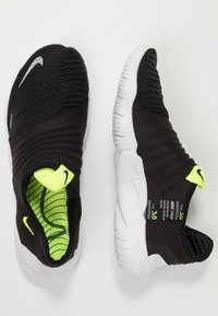 Czarne buty wsuwane z teksturowaną cholewką, białą gumową podeszwą i neonowozielonymi akcentami w środku. Posiadają srebrne logo Nike na nosku.