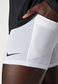 VITA idrottsshorts i vitt med svart Nike-logotyp, tillverkade av slätt, stretchigt material. Har en figurnära design och sömlös sömnad.