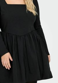 Svart langermet kjole med firkantet hals, med samlet stoff i livet og en utsvingt skjørt, laget av mykt, teksturert materiale.