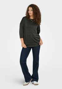 Sort, glitrende oversized top med trekvartærmer, parret med flagrende mørke denimjeans med kontrastsyning og hvide sneakers.
