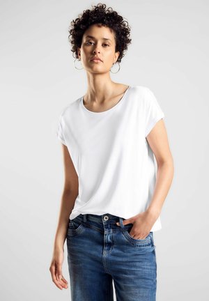 T-shirt bianco a maniche corte con scollo rotondo, abbinato a jeans blu. La maglietta ha una texture liscia, evidenziando un design semplice.