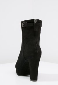 Black suede ankle boots with a thick heel, side zipper, and an adjustable buckle accent on the ankle. Smooth texture, modern design.