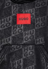 Felpa con cappuccio in nero e grigio, caratterizzata da un motivo testurizzato e un'etichetta rossa con la scritta "HUGO" in lettere nere. Tessuto morbido e vestibilità rilassata.