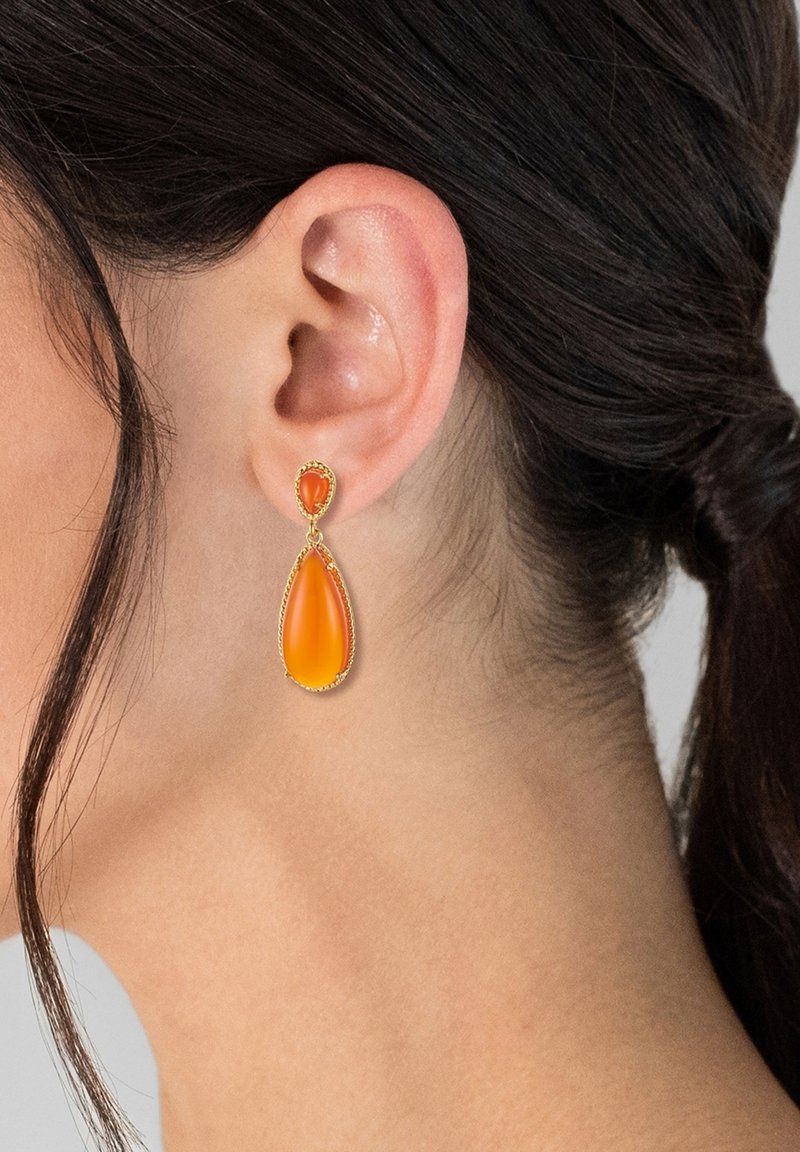 Goldfarbene Tropfohrringe mit einem Tropfen-Design, ausgestattet mit einem lebhaften orangefarbenen Stein und einem kleineren herzförmigen Akzent. Glatte Textur.