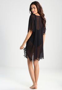 Black lightweight kaftan with short sleeves, sheer fabric, side slits, and pom-pom trim along the hem.
