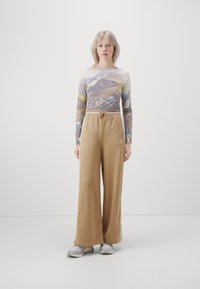 Top de manga larga con un estampado de montaña, combinado con pantalones de pierna ancha color beige que tienen cintura con cordón y aberturas laterales, usados con zapatillas grises.