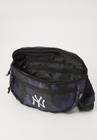 Sac bandoulière noir et bleu à motif camouflage, fabriqué en tissu durable. Il est doté de deux compartiments zippés et d'un logo blanc bien en vue.