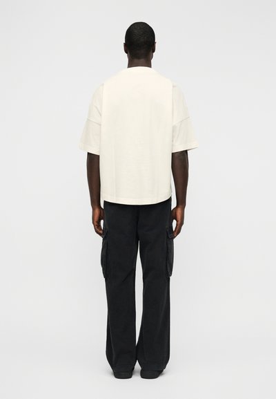 Χαλαρή, κοντομάνικη κρεμ μπλούζα και μαύροι παντελόνια cargo με πλευρικές τσέπες και άνετη σιλουέτα. Απλός, μινιμαλιστικός σχεδιασμός.