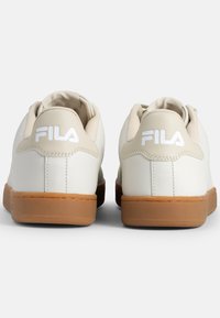Sneakers brancos em pele com um acabamento liso, apresentando uma sola de borracha gum e o logótipo da Fila em relevo no calcanhar. Design de bico redondo.