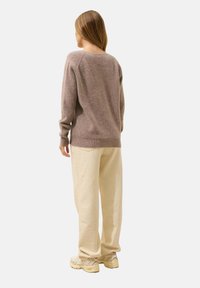 Brązowy, prążkowany sweter o luźnym kroju, zestawiony z luźnymi kremowymi spodniami. Tekstura wydaje się miękka i przytulna, bez widocznych wzorów.