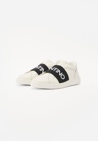 Sneakers bianchi in pelle con una cinghia elastica nera che presenta la scritta "VALENTINO" in lettere bianche. Texture liscia e design minimalista.