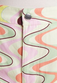 Tecido de algodão leve com um padrão ondulado em cores pastel: verde, rosa, laranja e creme, com detalhes em botão prateado.