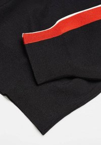 Mustat neulotut neuleet, joissa on punavalkoinen raitaakseli kauluksen ympärillä. Kangas näyttää sileältä ja keskipainoiselta.