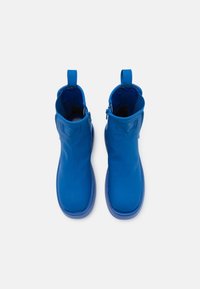 Une paire de bottines bleues vives avec des fermetures éclair latérales et des pattes de tirage, vues d'en haut sur un fond blanc.