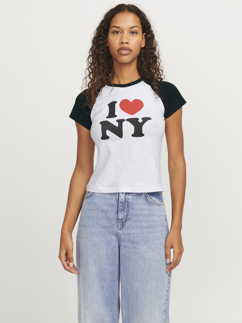Balts īsais t-krekls ar melniem raglanu piedurknēm. Iekļauj drosmīgu "I ❤️ NY" grafiku melnā un sarkanā krāsā. Kombinēts ar gaišas krāsas platām džinsu biksēm.