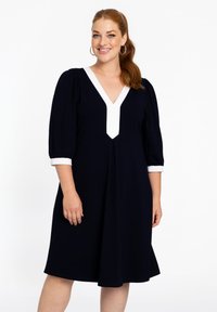 Marineblaues Kleid mit einem weißen V-Ausschnitt und Ärmeln. Verf�ügt über Puffärmel und einen ausgestellten Saum, hergestellt aus einem glatten, leichten Stoff.