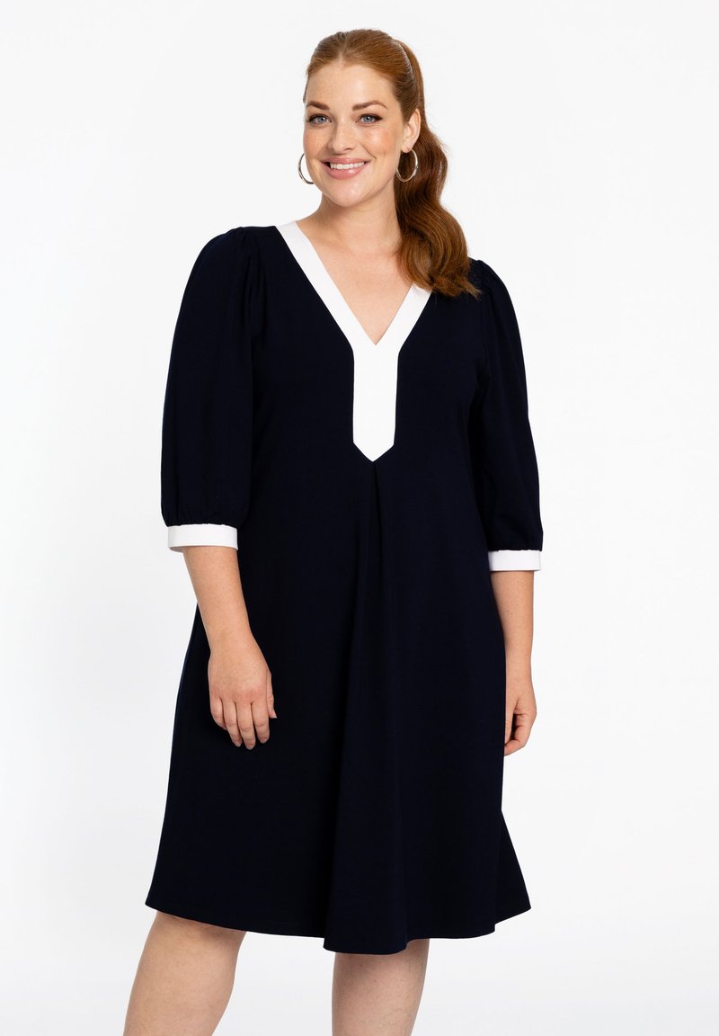 Marineblaues Kleid mit einem weißen V-Ausschnitt und Ärmeln. Verfügt über Puffärmel und einen ausgestellten Saum, hergestellt aus einem glatten, leichten Stoff.