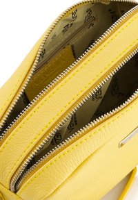 Gelbe Lederhandtasche mit drei Reißverschlussfächern, strukturiertem Obermaterial, kontrastierenden Nähten und einem bedruckten Innenfutter.
