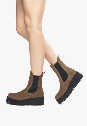 Stivali alla caviglia in suede marrone con pannelli elastici neri ai lati e suole nere spesse, dotati di punta arrotondata e linguetta posteriore per facilitarne l'indossamento.